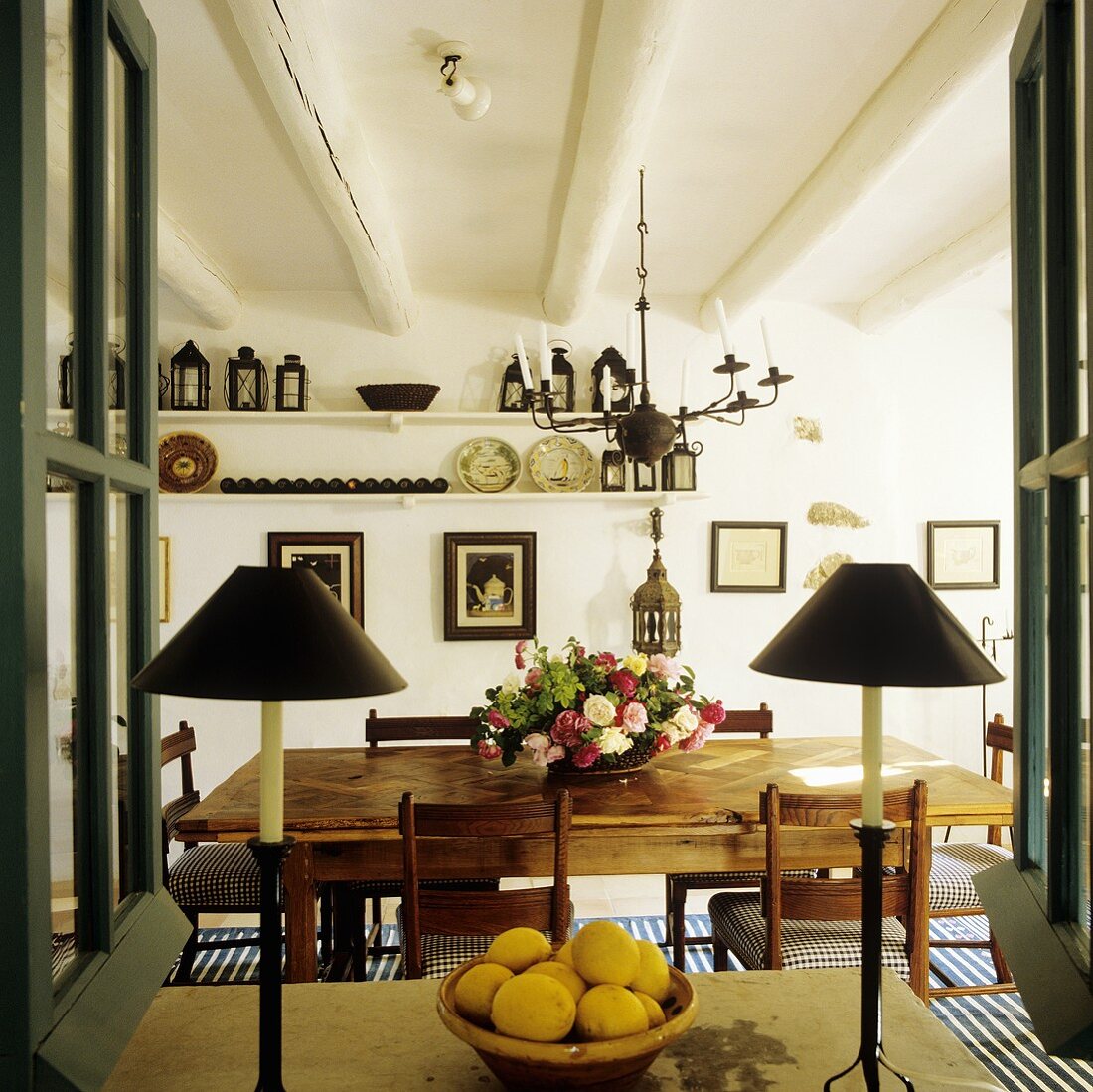 A view through a window onto table lamps and a dining table in a rustic country house