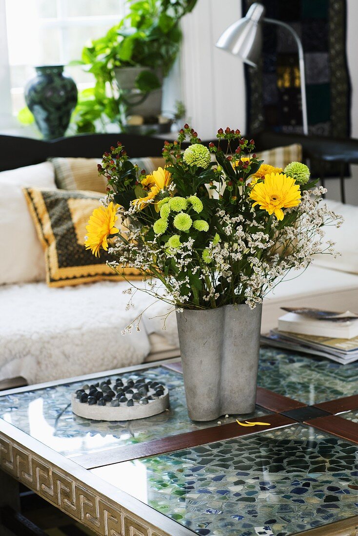 A bunch of flowers in a metal vase on a coffee table