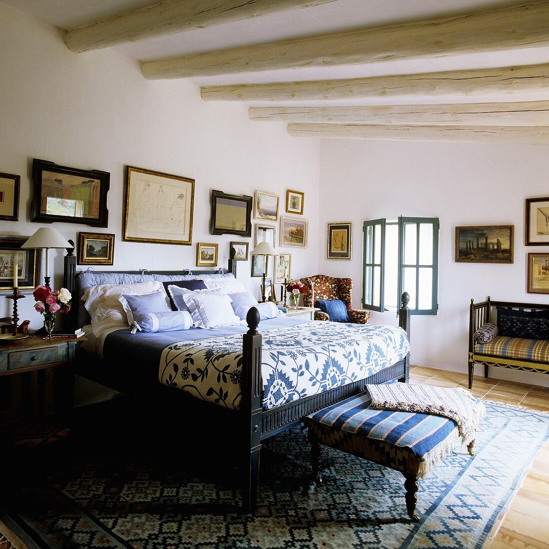 A bed with a blue and white quilt and an upholstered bench in a bedroom in Mediterranean country house with a wood beam ceiling