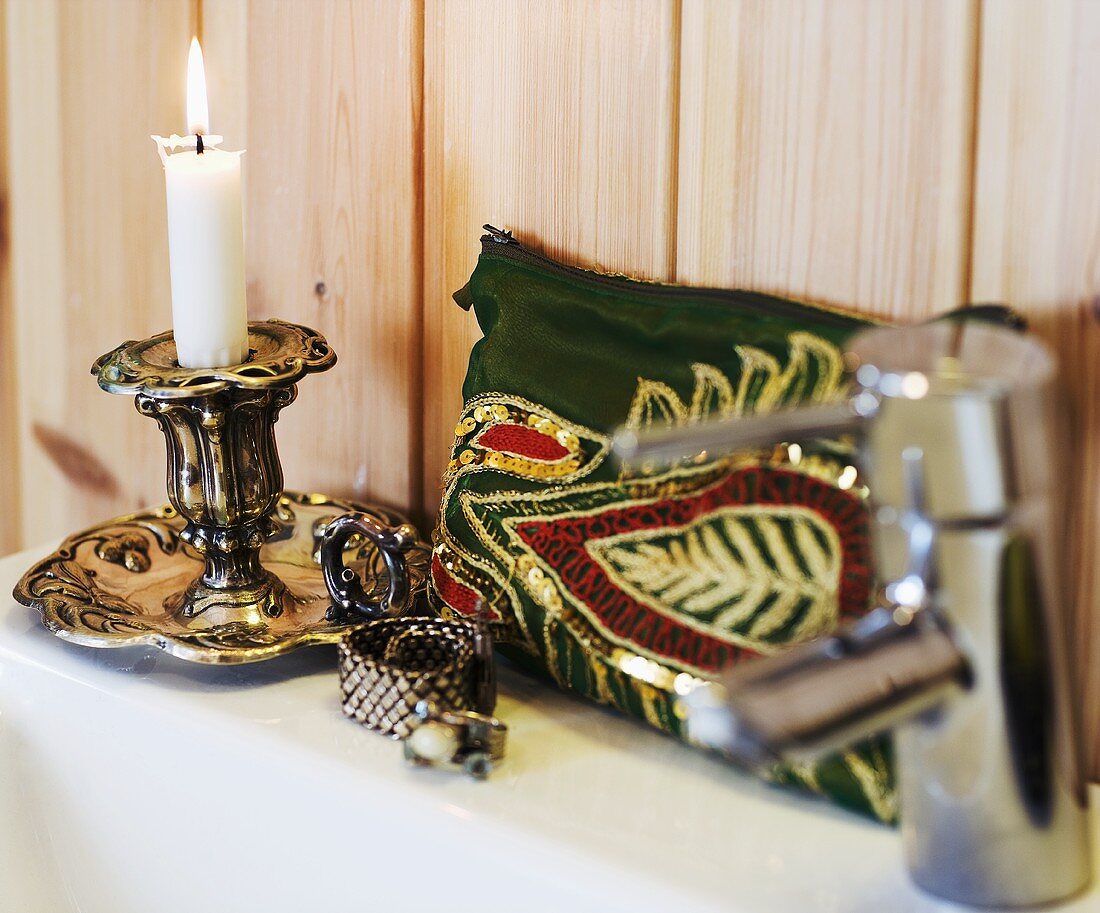 A candlestick with a burning candle and a make-up bag