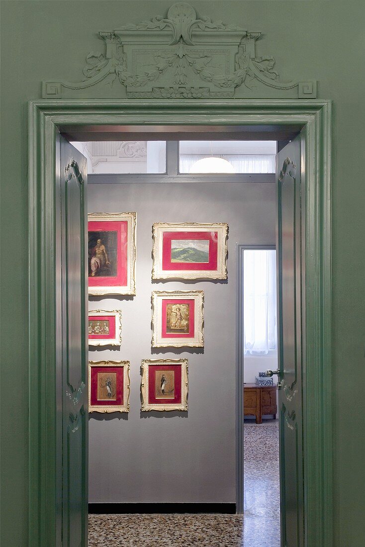 A view through a double door onto a collection of pictures hanging on the wall in red mounts