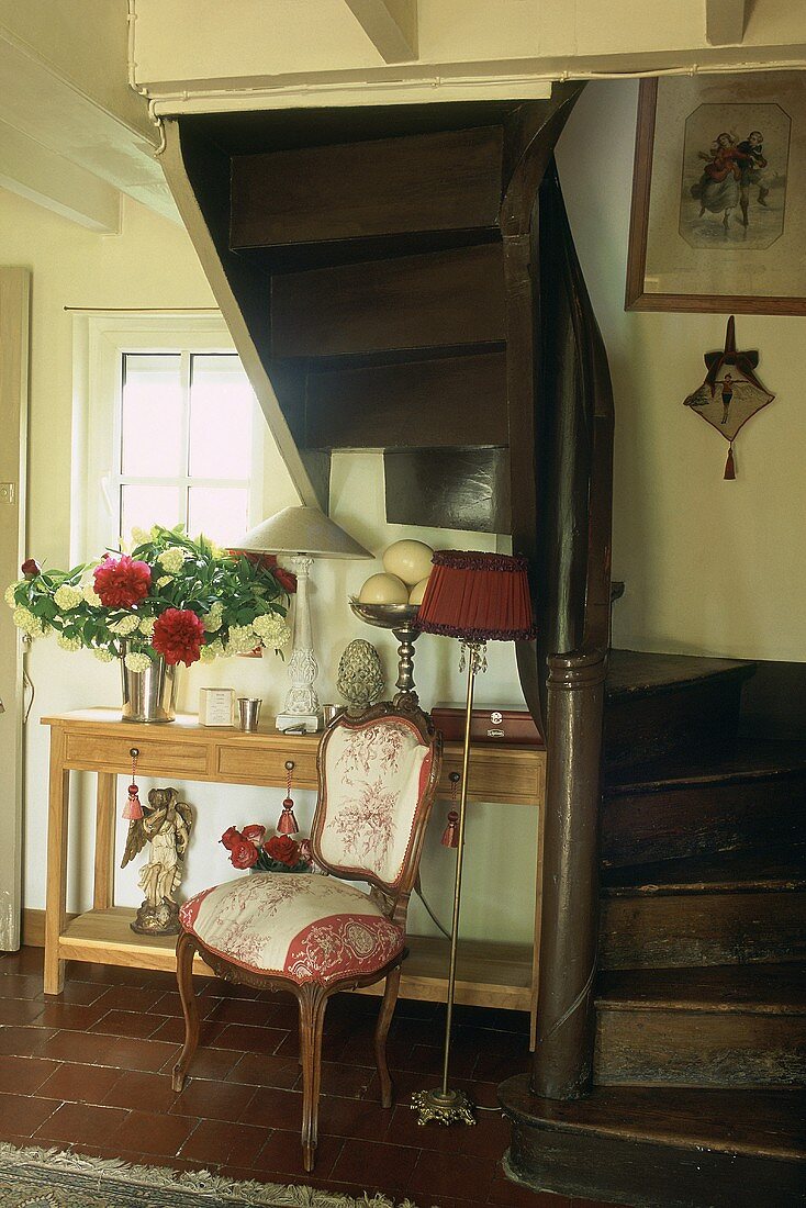 A dark wooden staircase with an upholstered baroque chair and a wall table in niche