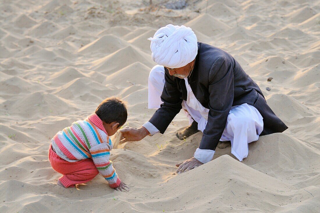 India, Rajasthan, Pipasar, Bishnoi elder and grandson building small sand dunes in the temple courtyard  Pipasar is Guru Jambeshwars birthplace and a major site of pilgrimage for the Bishnoi community