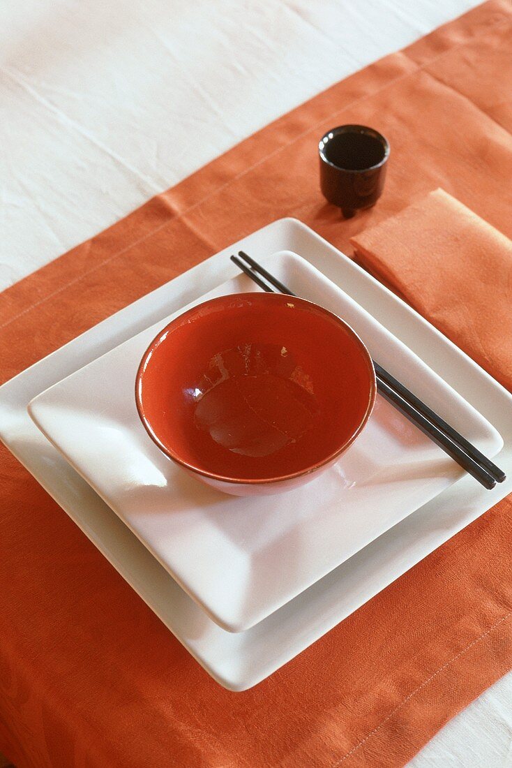 An Oriental place setting with a red bowl on white plates with chopsticks