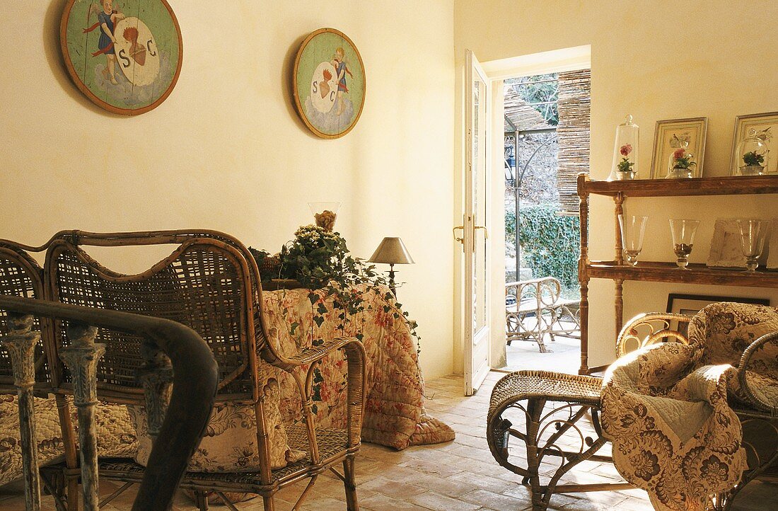 Wicker furniture with cushions and a wall shelf with vases in a country house-style living room and a view through an open garden door