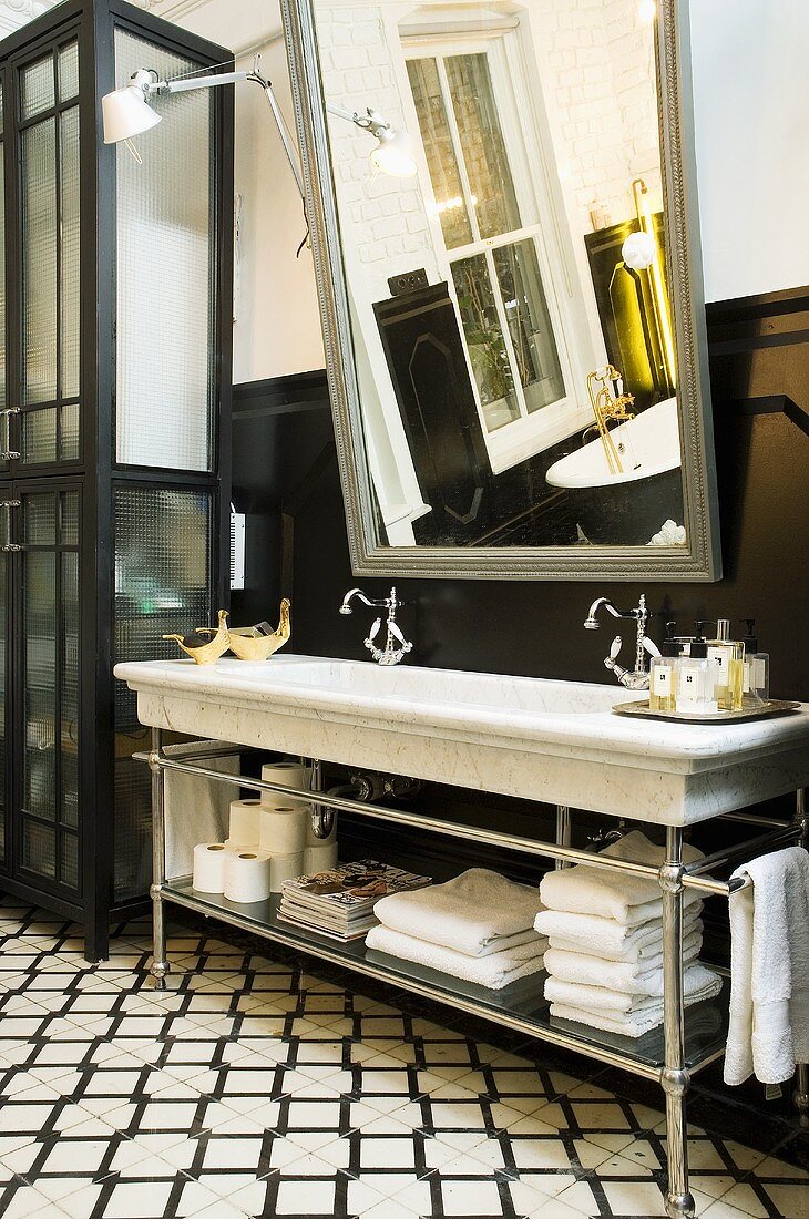 A wash stand with a marble basin and a mirror in front of a black panelled wall