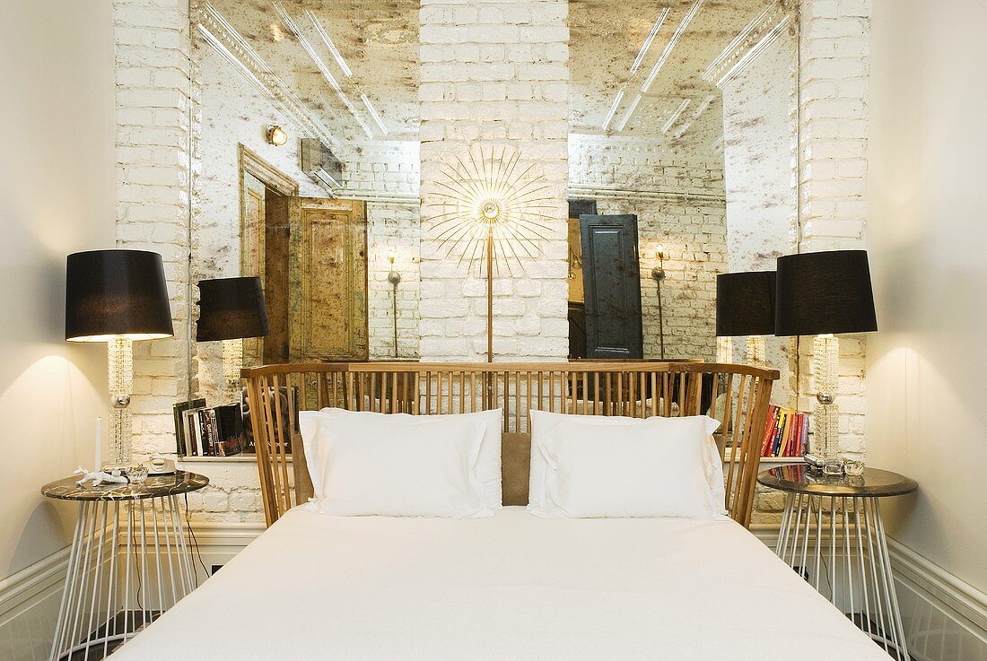 A double bed with a wood slat head rest against a white painted brick wall and floor-to-ceiling mirrors