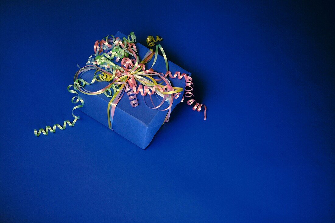 Blue gift wrapped present with colorful ribbons on a blue background