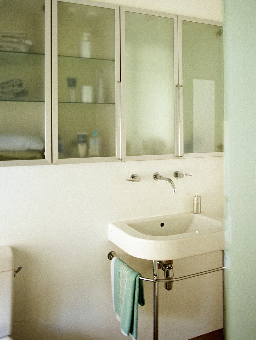 Bathroom with washbasin on chrome stand and glass fronted cupboards.