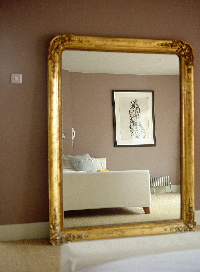 Large gold painted framed mirror against brown wall reflecting bed