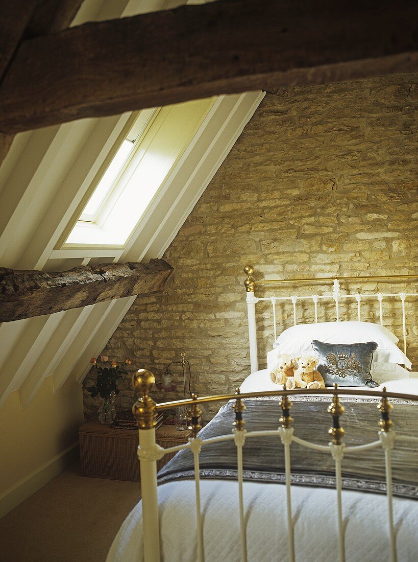 Brass bed with teddy bears under a pitched attic roof and skylight.