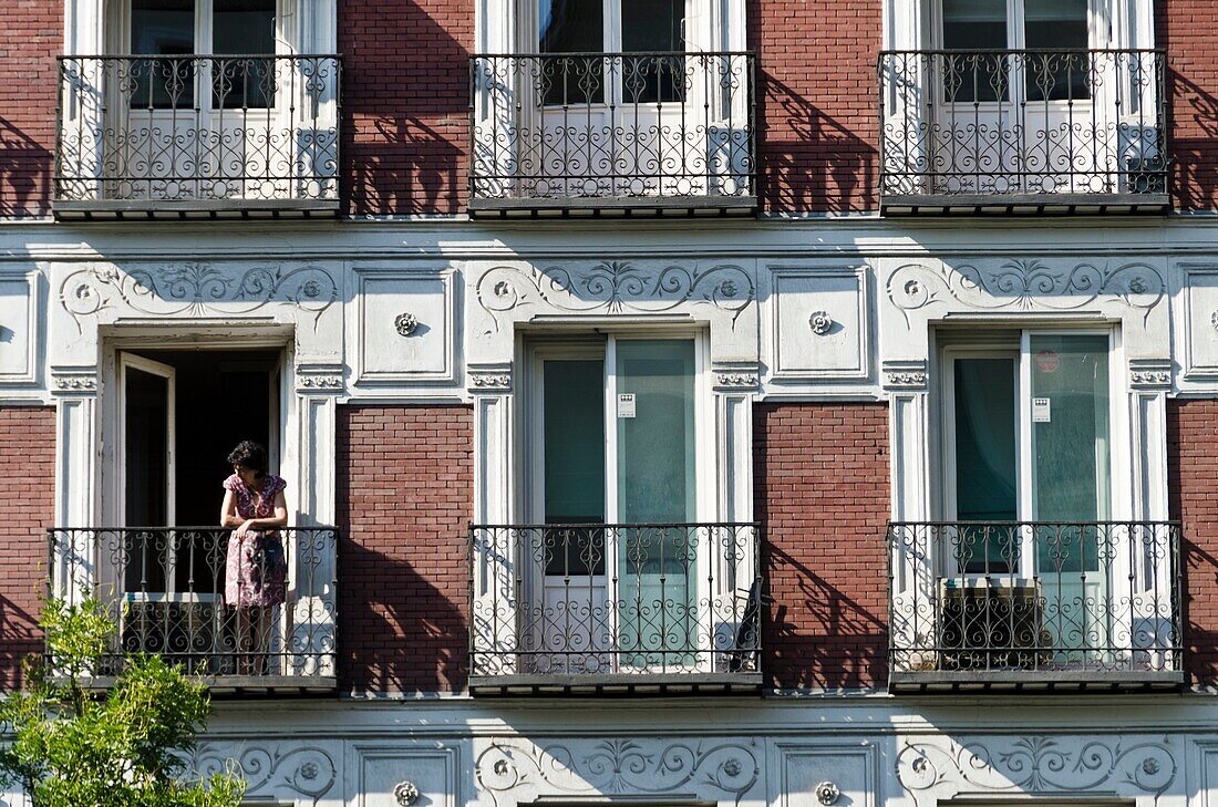 Woman look at from her balcony. Building Facade at Alcala street, Madrid, Spain
