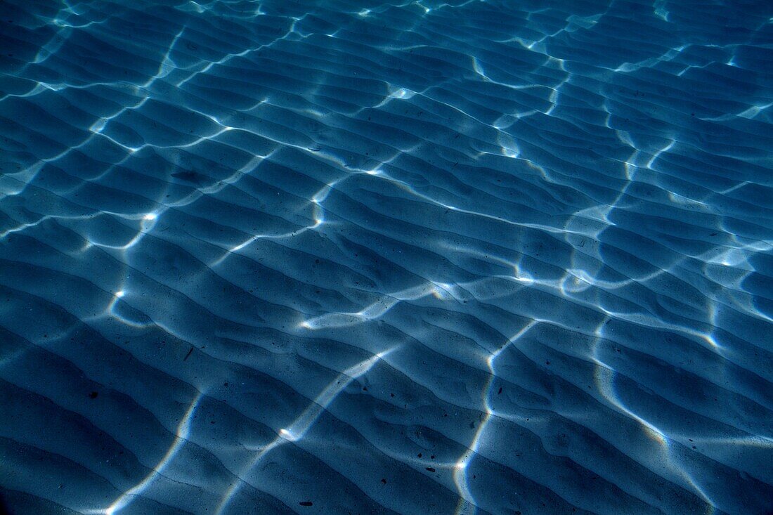 Sunlight forming mosaic shapes on a sandy ocean floor.