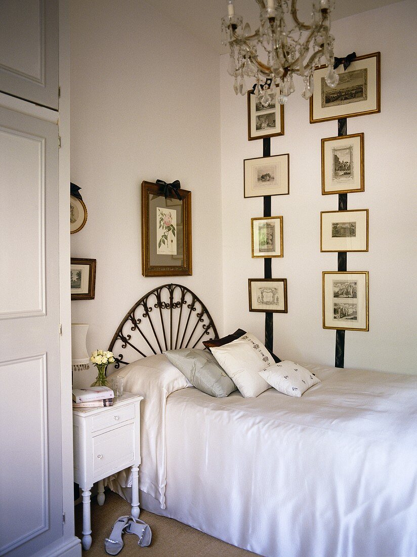 Artworks displayed on wall above single bed with ornate arched headboard