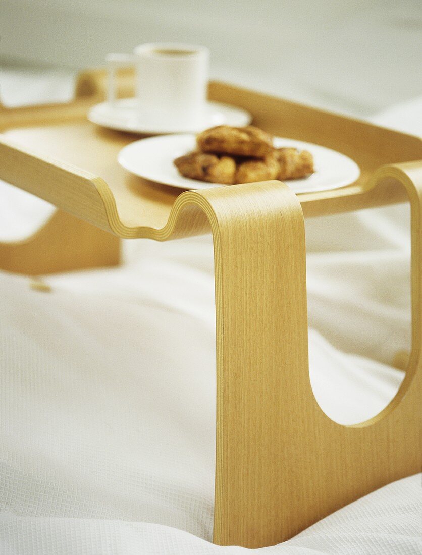 A detail of a wooden breakfast tray on a bed, plate of croissants and white cup and saucer,