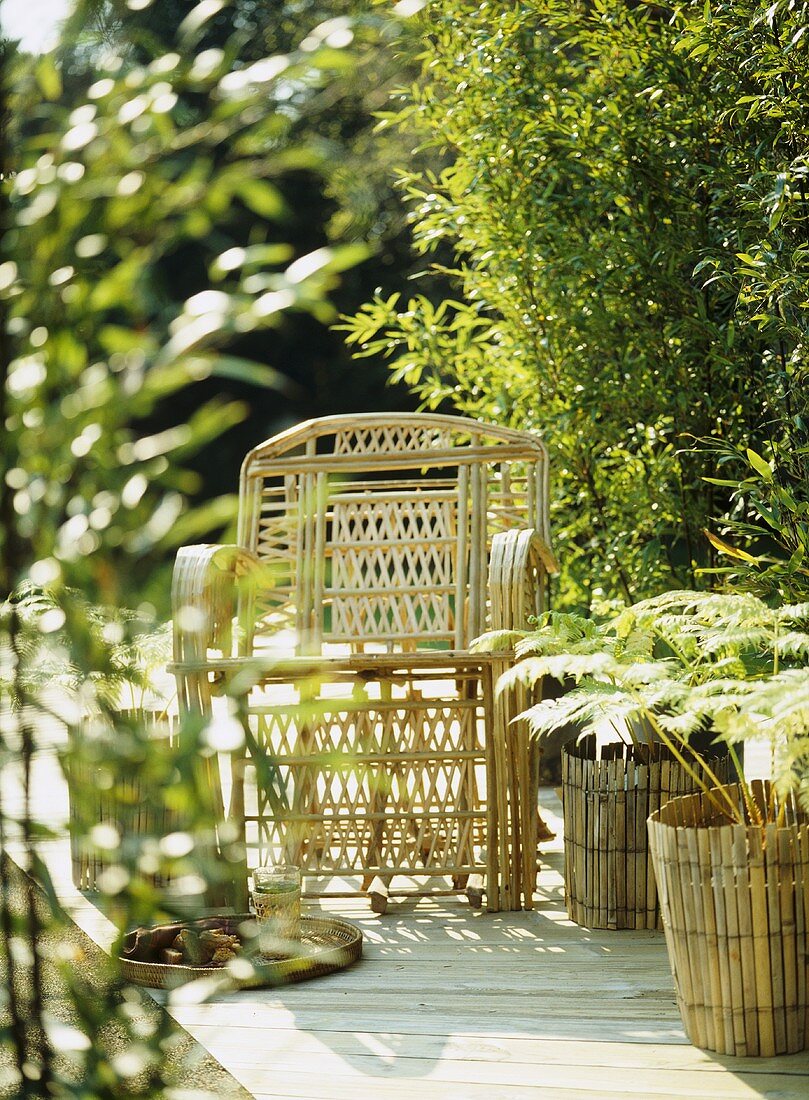 A detail of a decked garden patio, showing a bamboo cane chair and plant containers