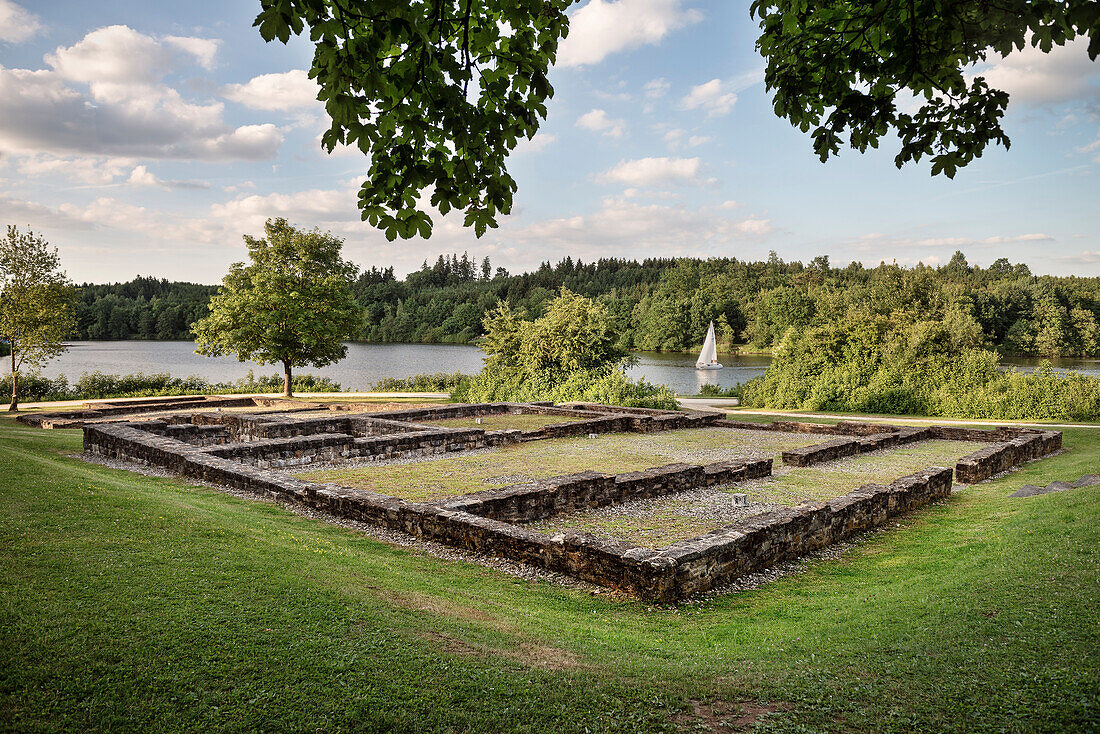 Ruins of a bathhouse in front of a lake with sailing boat passing by, Limes (border wall of Roman Empire) Park Rainau-Buch, Aalen, Ostalb province, Swabian Alb, Baden-Wuerttemberg, Germany, UNESCO world heritage site