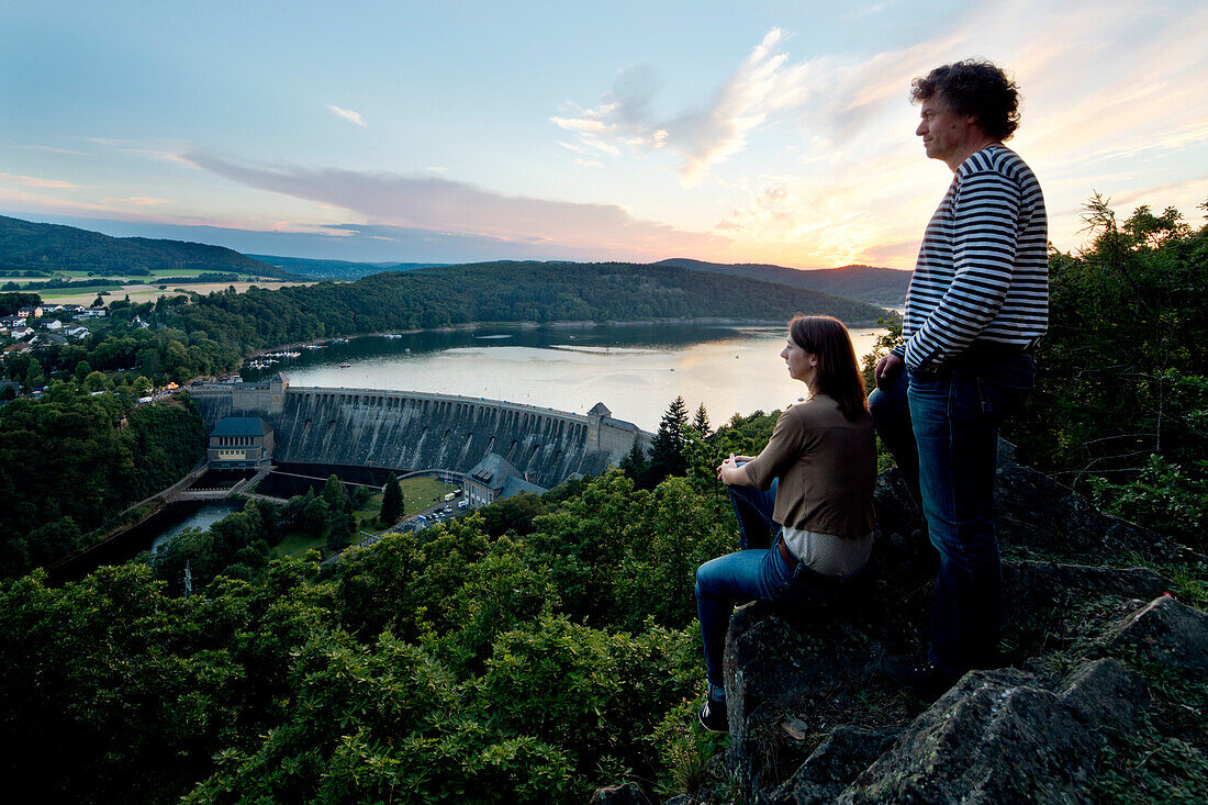 Two people enjoying the view of Edertalsperre dam at Lake Edersee in Kellerwald-Edersee National Park at sunset, Lake Edersee, Hesse, Germany, Europe