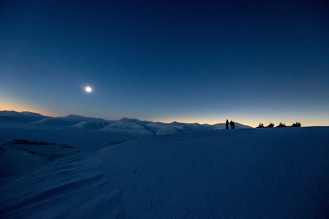 3 Personen mit Schneemobilen in winterlicher Landschaft erleben die totale Sonnenfinsternis auf Spitzbergen, Svalbard, Norwegen