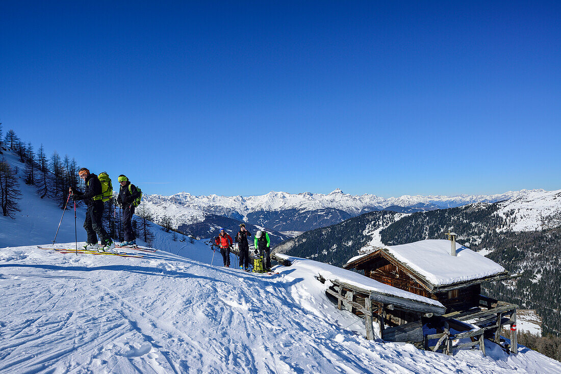 Several persons back-country skiing having a break at an alpine hut, Stubai Alps in the background, Gammerspitze, valley of Schmirn, Zillertal Alps, Tyrol, Austria