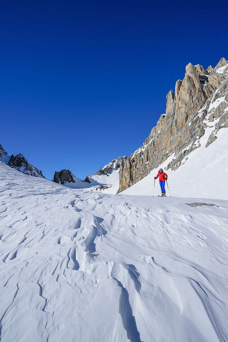 Frau auf Skitour steht unter den Felswänden des Monte Sautron, Valle Maira, Cottische Alpen, Piemont, Italien