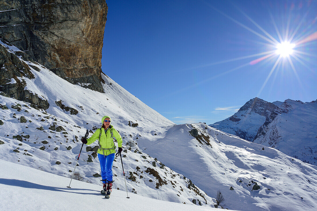 Woman back-country skiing ascending beneath rock wall towards Monte Salza, Monte Salza, Valle Varaita, Cottian Alps, Piedmont, Italy