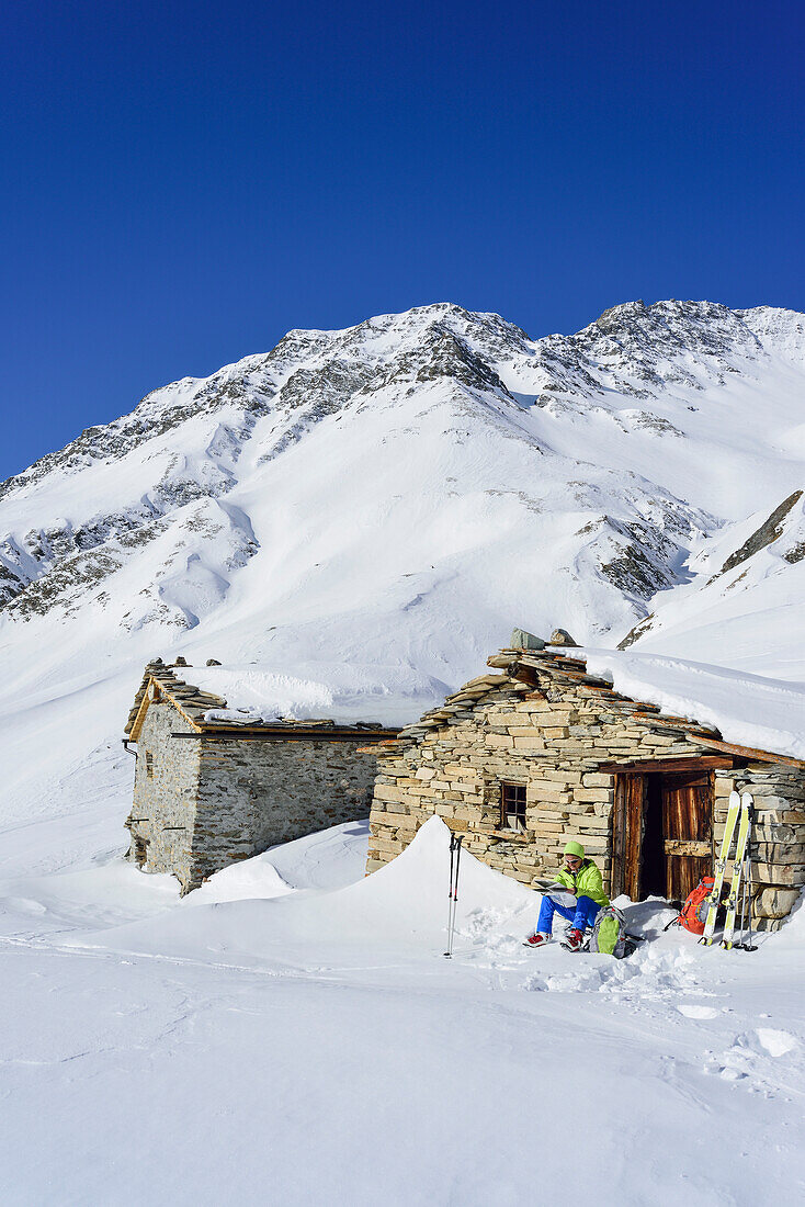 Frau auf Skitour macht an Almhütten Pause, Monte Salza, Valle Varaita, Cottische Alpen, Piemont, Italien