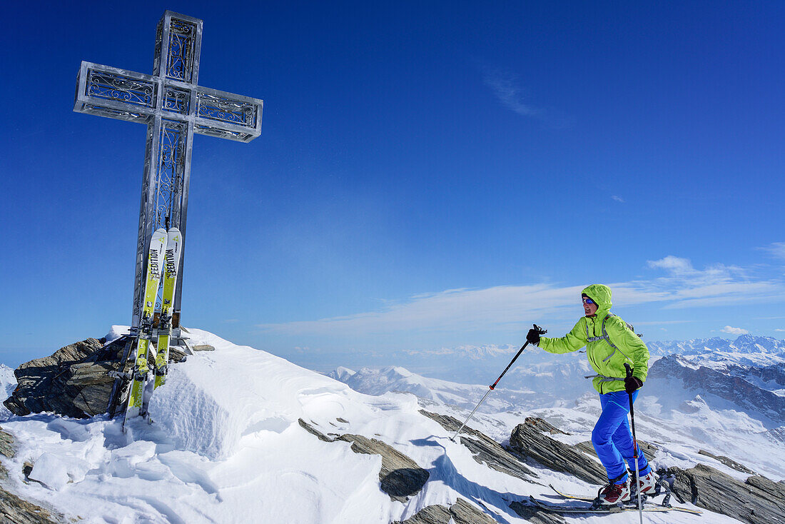 Woman back-country skiing ascending towards cross at summit of Monte Salza, Monte Salza, Valle Varaita, Cottian Alps, Piedmont, Italy