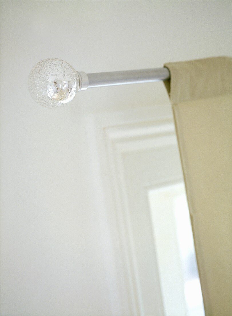 A detail of light fabric curtains hung upon a metal curtain rod with a silver ball finial