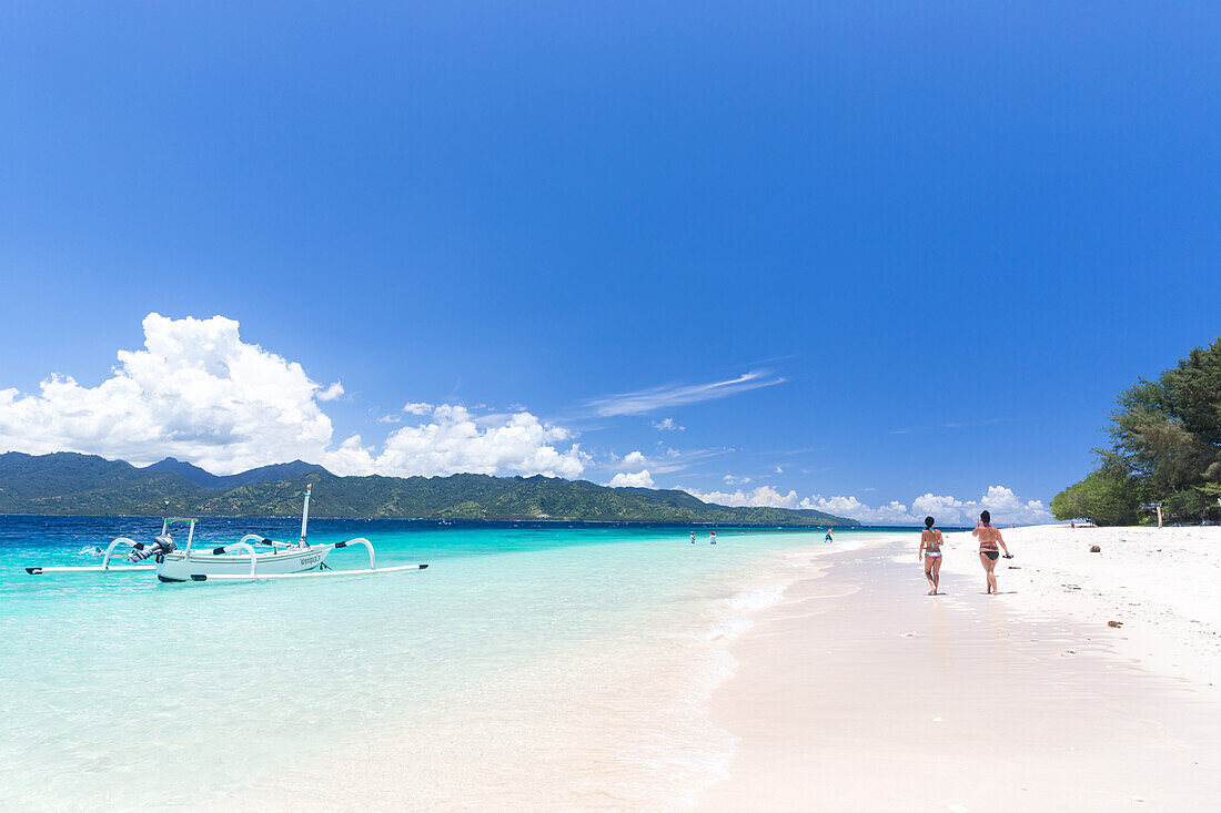 Two women walking along white sandy beach, Gili Meno, Lombok, Indonesia