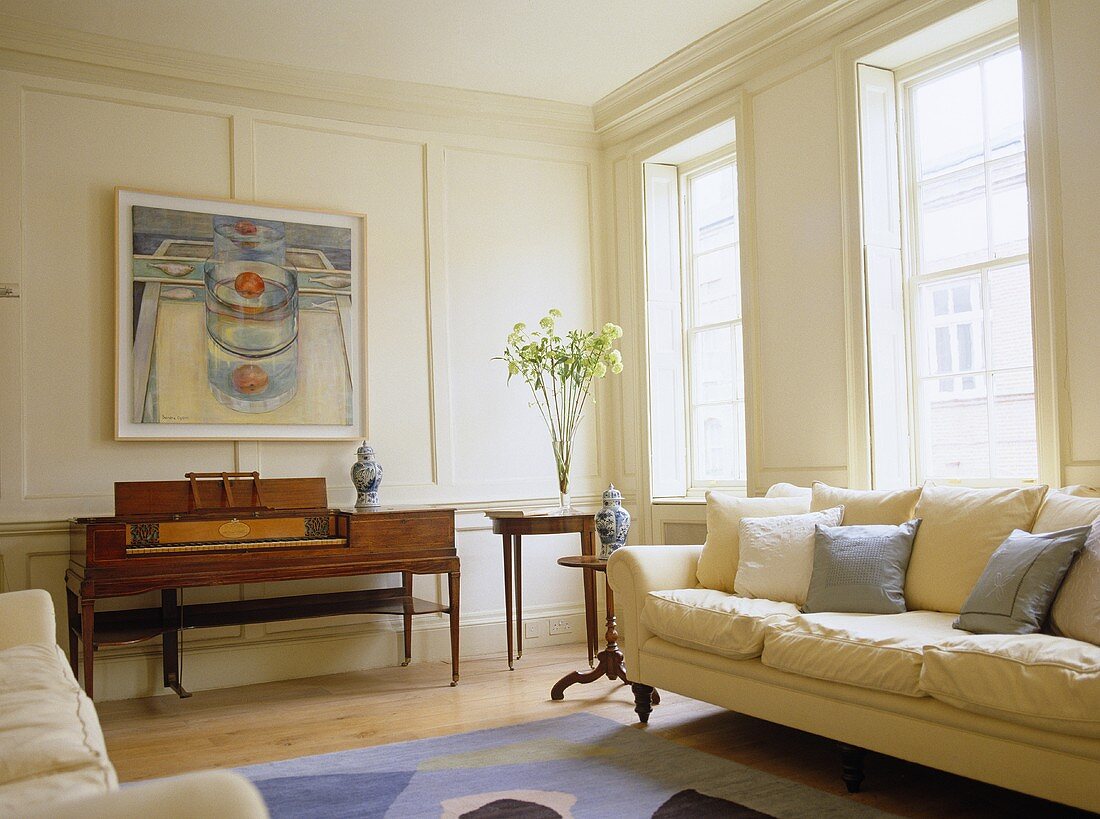 Sitting room with white panelled walls, cream sofa and antique piano.
