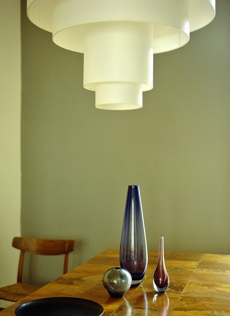 Three purple glass vases on wooden table with retro ceiling light above