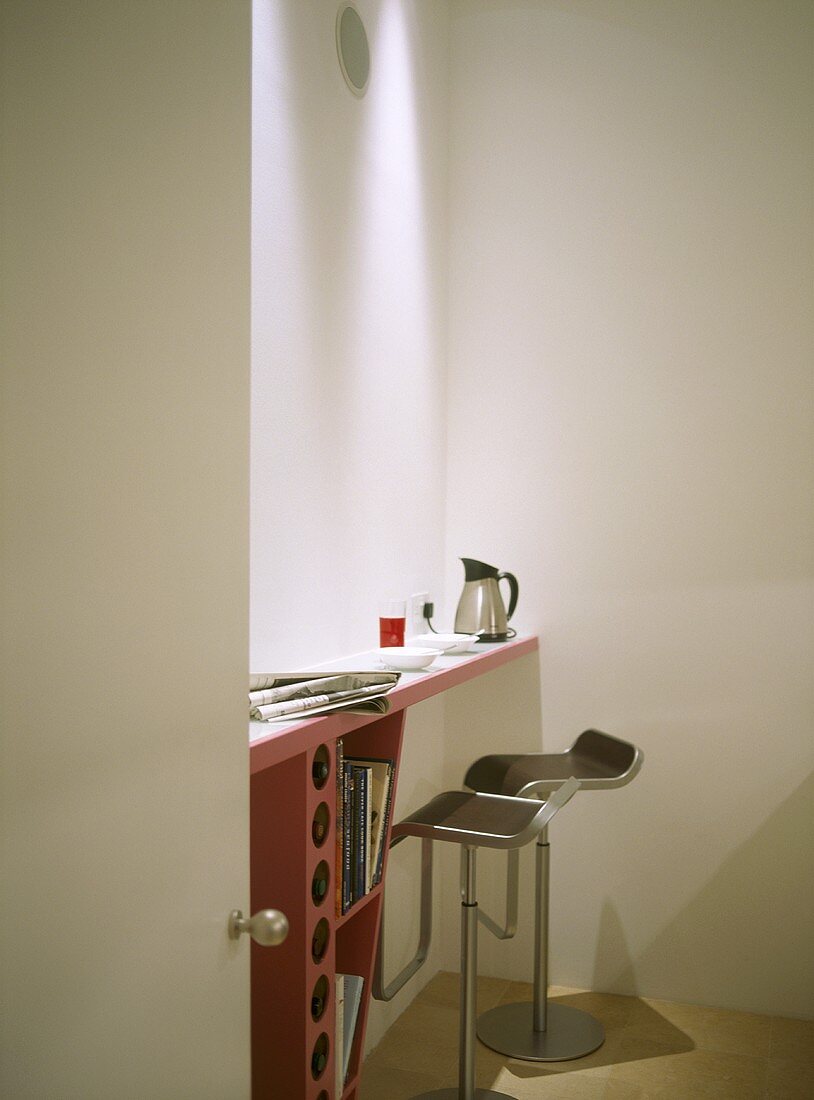 A detail of a modern kitchen in neutral colours, showing a breakfast bar area, pair of steel stools, seen through open door,
