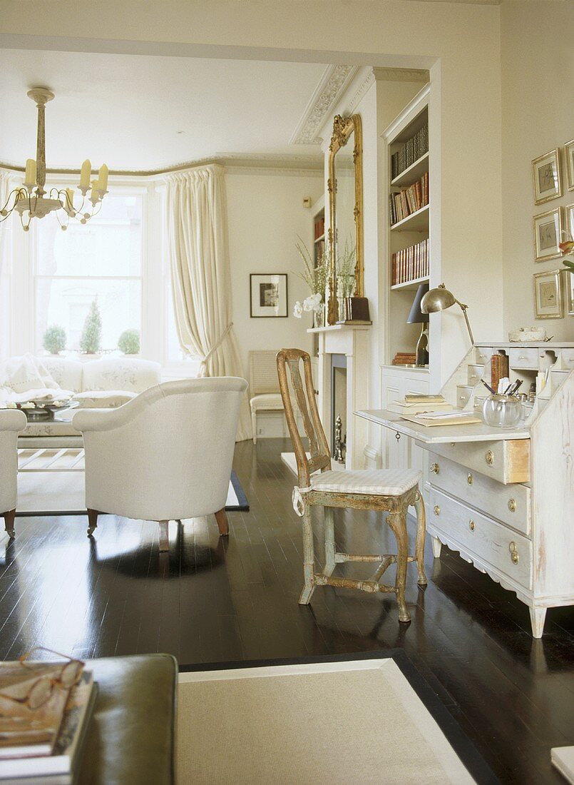 A traditional, white sitting room, polished wood floor, painted bureau, gilt chair, upholstered armchair,