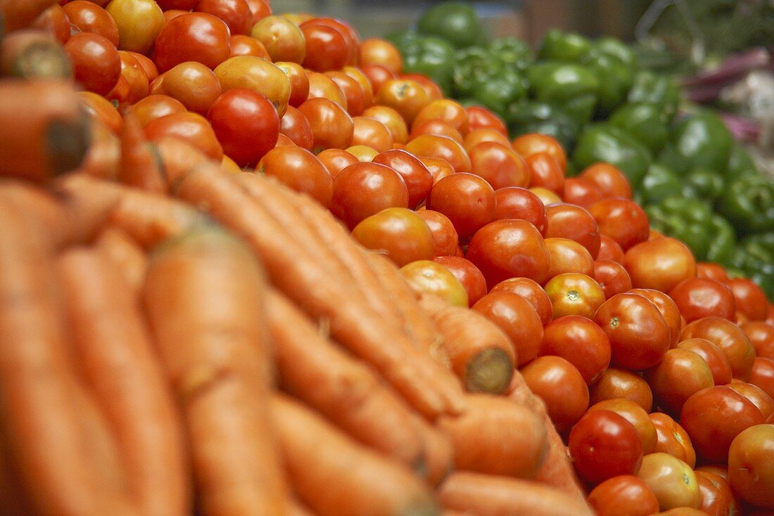 Eine Gemüseauslage mit frischen Möhren, Tomaten und grünen Paprikaschoten