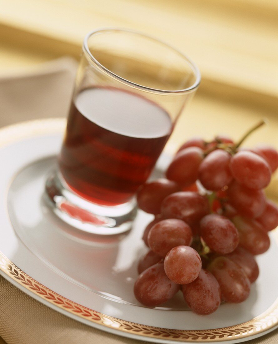 Glas Rotwein und rote Trauben auf Teller