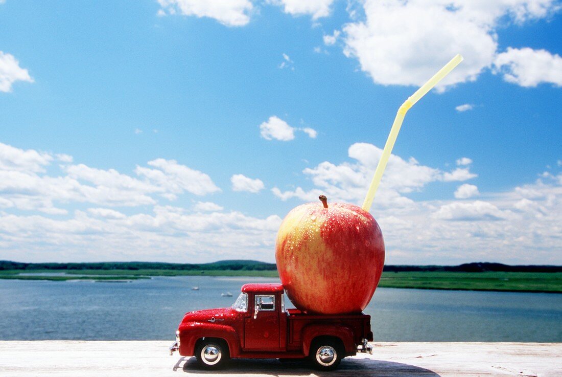 Apfel mit Strohhalm auf Modelllastwagen am Meer