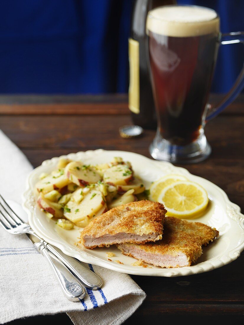 Paniertes Schweineschnitzel mit Kartoffelsalat, im Hintergrund Bier