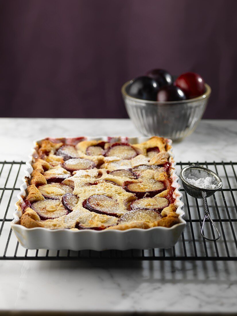Whole Plum Tart in a Baking Dish on a Cooling Rack