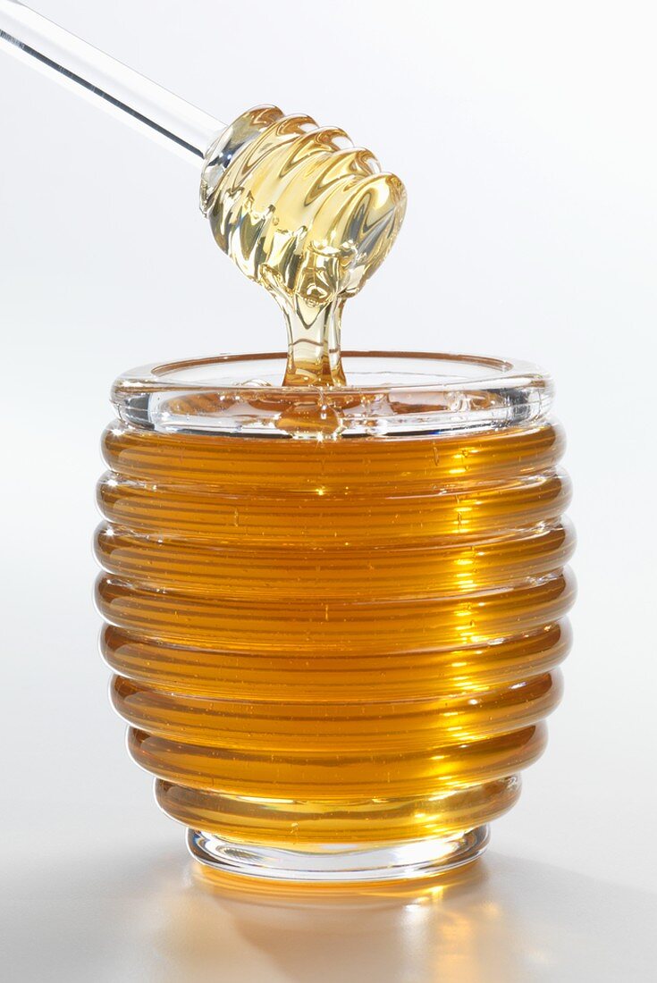 Honig tropft vom Honigheber in Glas