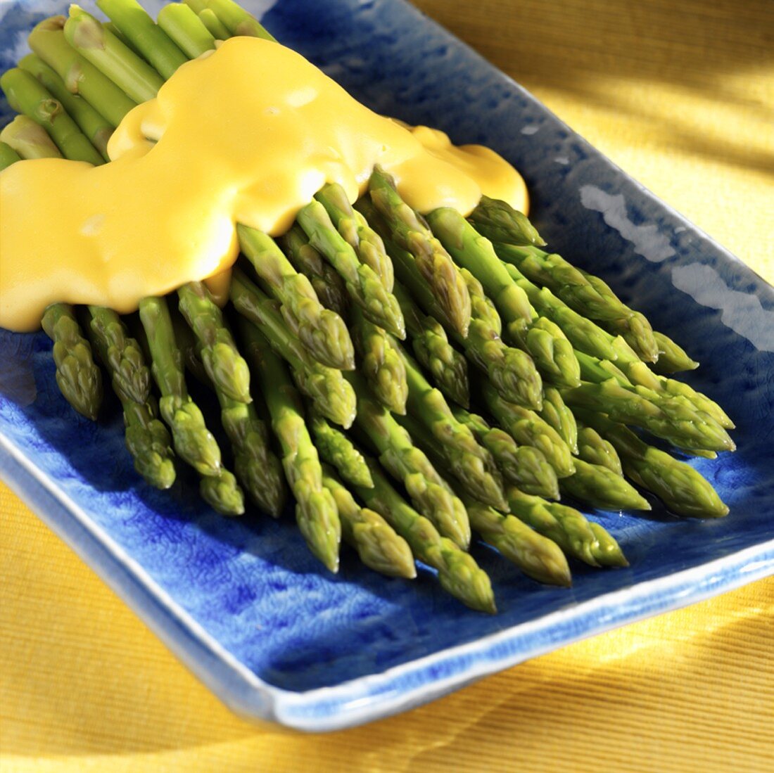 Cooked Asparagus on a Blue Serving Plate with Cheese Sauce