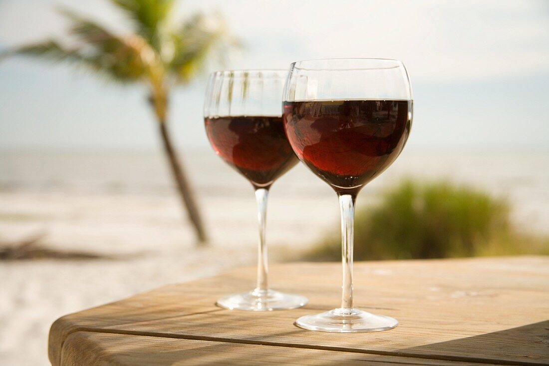Zwei Rotweingläser auf Holztisch am Strand