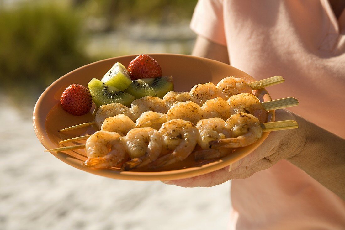 A Woman Holding a Plate of Skewered Shrimp at the Beach