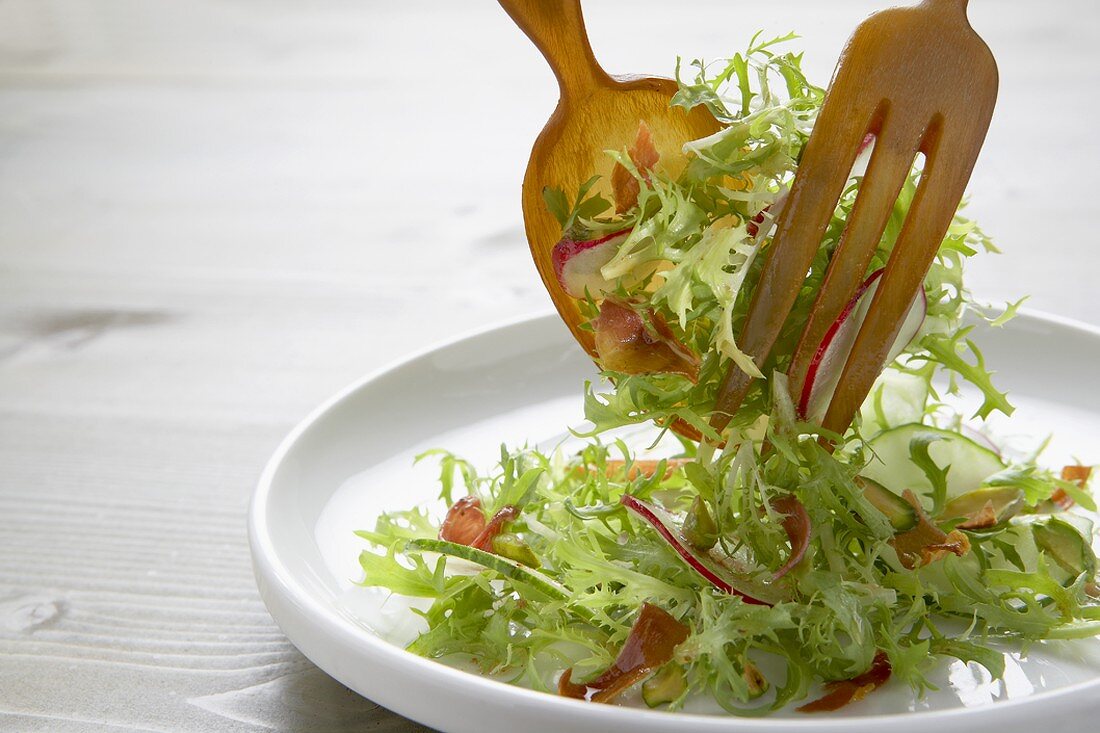 Friseesalat mit Salatbesteck auf Teller geben