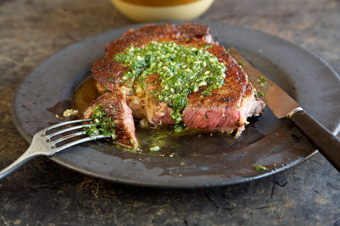 Rib Eye Steak Topped with Herb Sauce on a Plate, Sliced