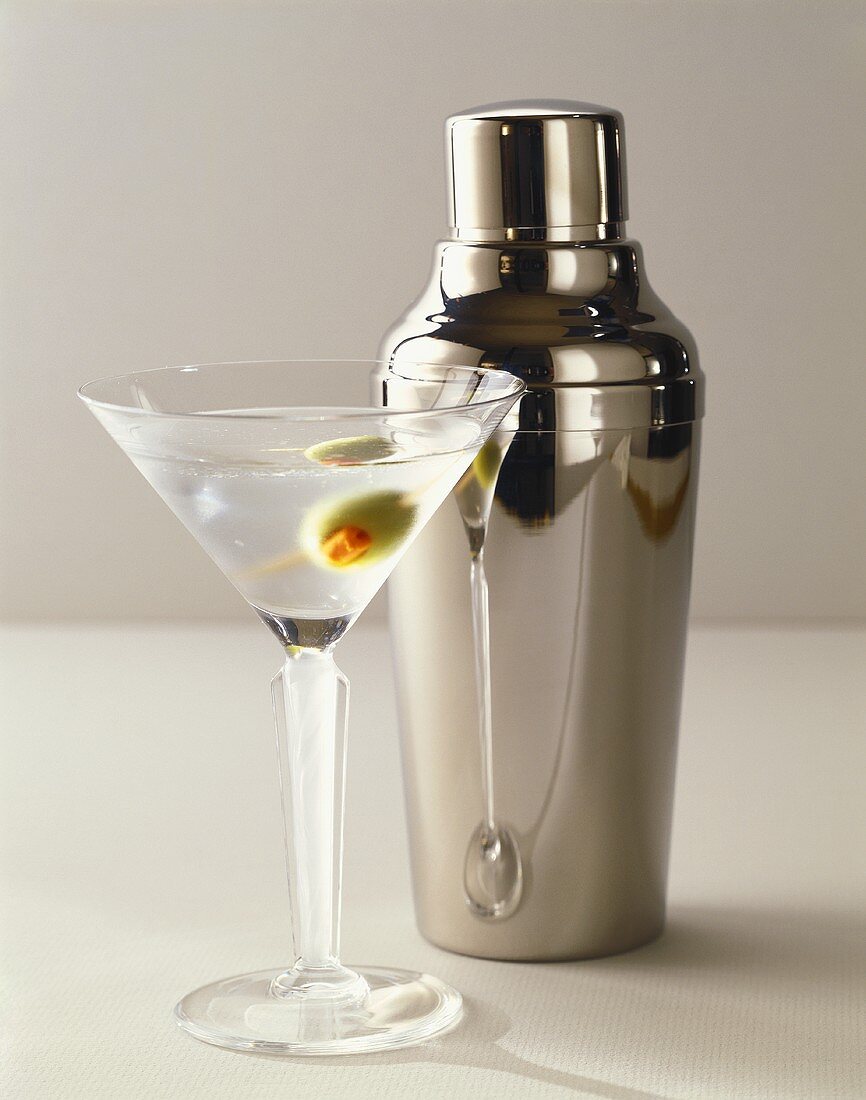 Martini mit Olive im Glas vor Cocktailshaker