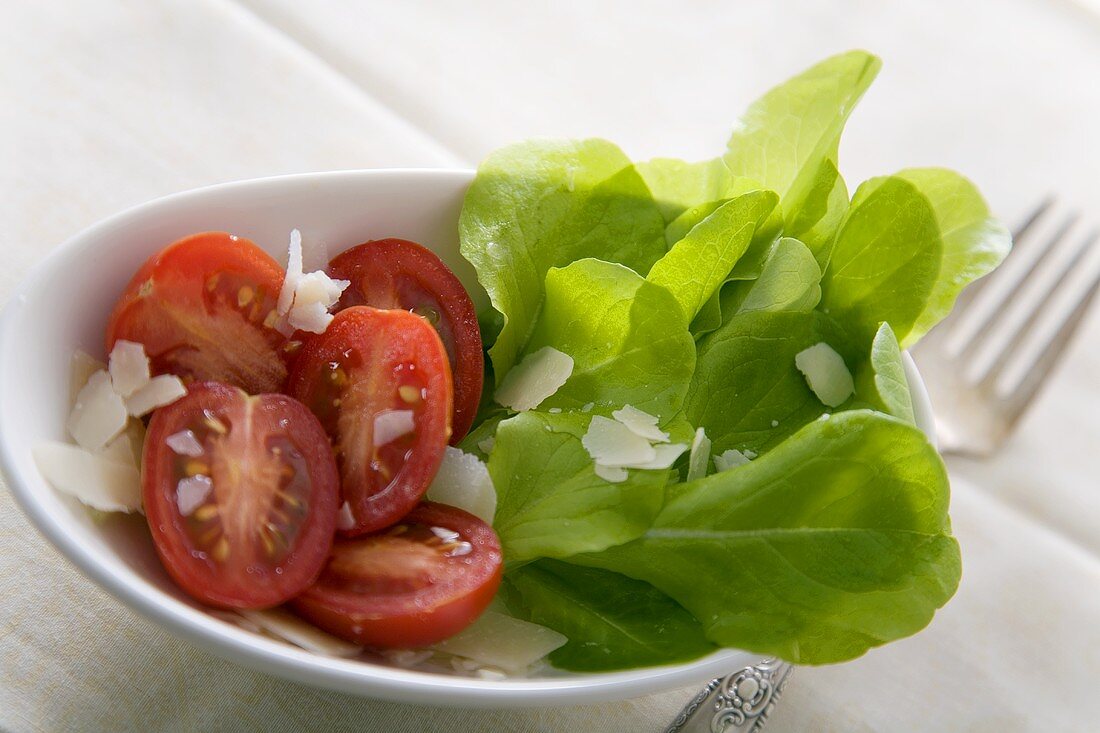 Ein Beilagensalat mit grünem Blattsalat, halbierten Tomaten und Parmesanspänen