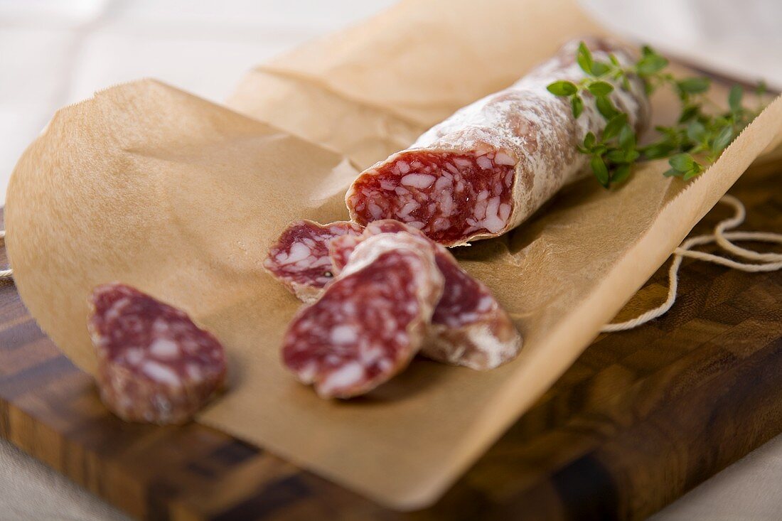 Partially Sliced Stick of Salami on Brown Paper; Cutting Board