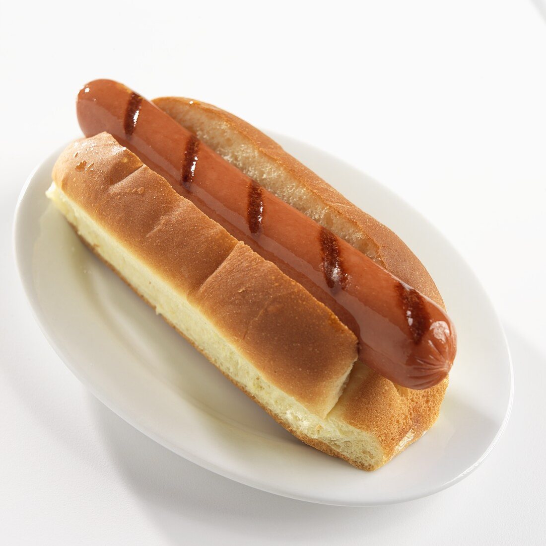Ein gegrillter Hot Dog im Brötchen auf einem weißen Teller