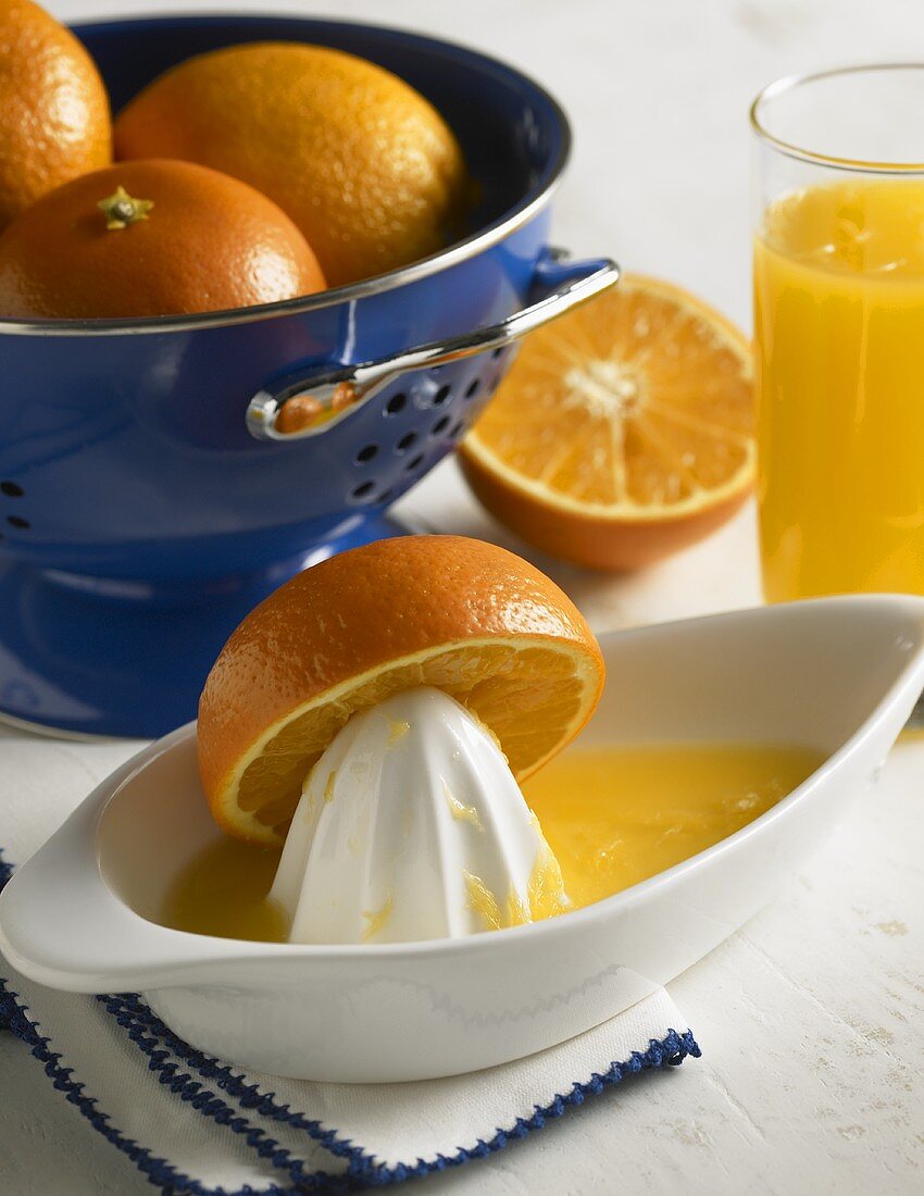 Orangen in Küchensieb, Saftpresse & Glas mit Orangensaft
